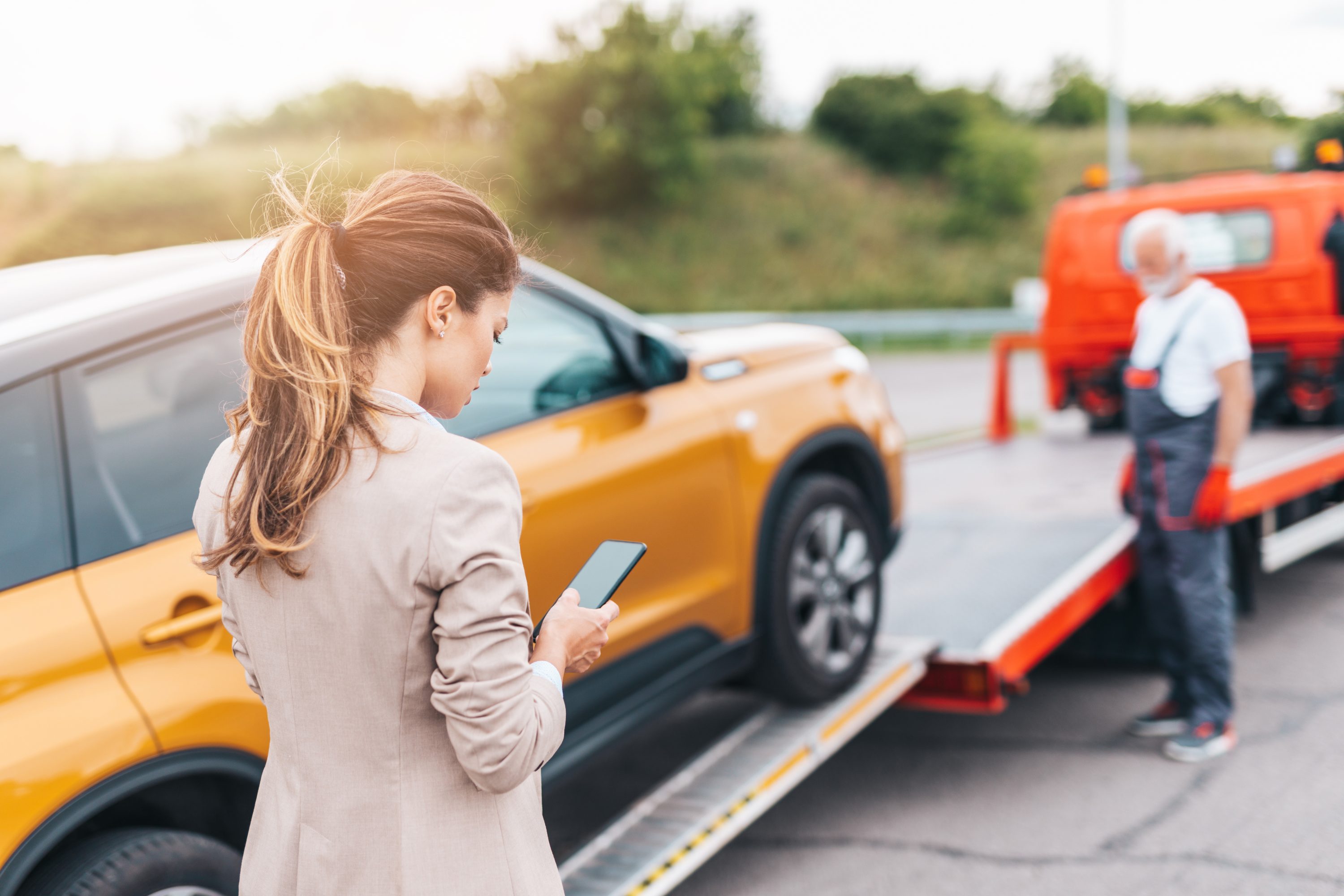 Elegant middle age business woman calling someone while towing service helping her on the road. Roadside assistance concept.